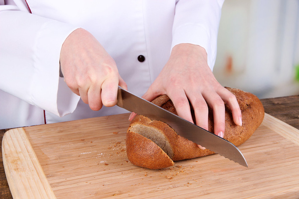 Cutting bread on wooden board on bright background - 写真・画像