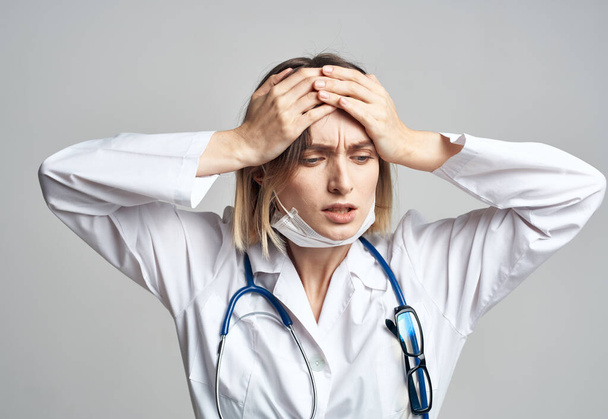 kobieta lekarz w masce medycznej trzymając się za ręce w pobliżu twarzy niebieski stetoskop przycięty widok - Zdjęcie, obraz