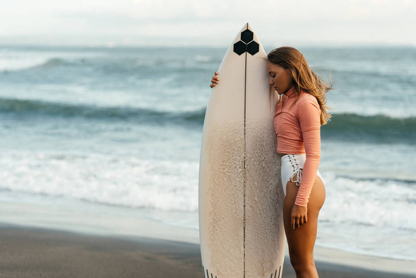 Young attractive surfer woman with white board at sunset on the ocean. Bali Indonesia. - Foto, Imagen