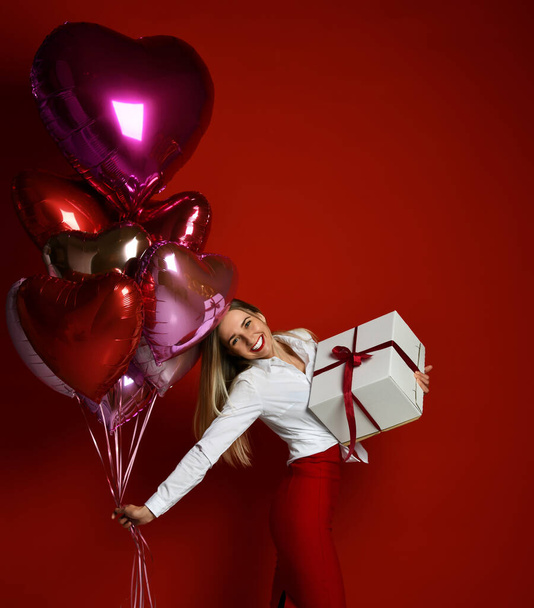 Happy, feeling love blonde woman in white blouse and red skirt walks with big gift box and colorful balloons in hand - Foto, Bild