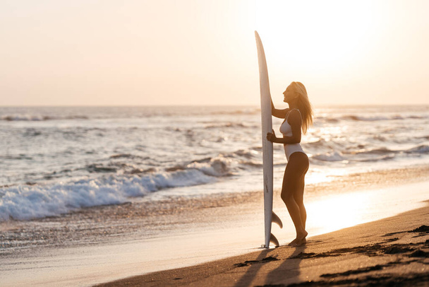Beautiful surfer woman on the beach at sunset - 写真・画像