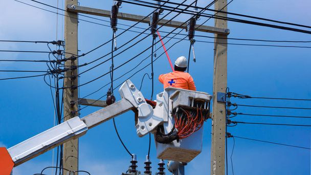 Low angle view of electrician with disconnect stick tool on crane truck are working to install electrical transmission on power pole against blue sky - Photo, Image