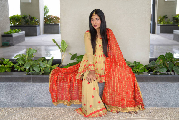 Νεαρή γυναίκα φοράει παραδοσιακό ινδικό φόρεμα ενώ κάθεται - Φωτογραφία, εικόνα