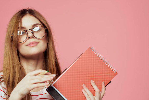 Молодая студентка с книгами на розовом фоне в очках в институте лицевого образования обрезанный вид - Фото, изображение