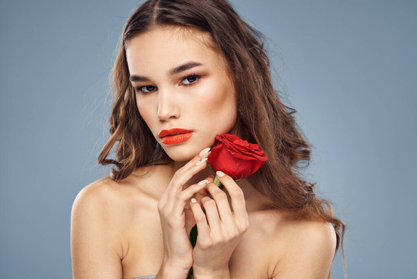顔の近くに赤いバラを持つ女性の肖像画灰色の背景とメイク巻き毛 - 写真・画像