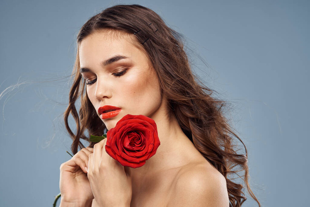 Portrét ženy s červenou růží v rukou na šedém pozadí nahá ramena večerní make-up - Fotografie, Obrázek