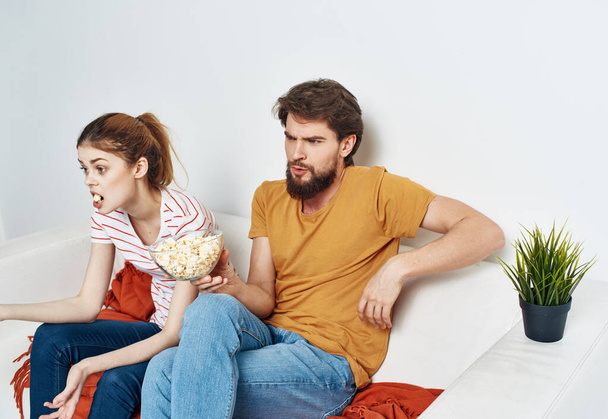 Мужчина и женщина на диване смотрят телевизор с попкорном в тарелке - Фото, изображение