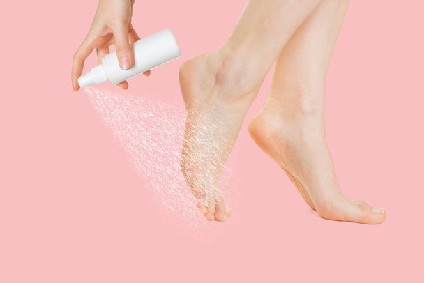 Pernas femininas mostradas no perfil e uma mão que pulveriza cosméticos ou medicamentos no pé. Fundo rosa. Fecha. O conceito de frescura, hidratação e proteção da pele dos pés. - Foto, Imagem