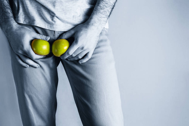 Mies beige farkut tasolla sukupuolielimissä, pitämällä kypsä ja mätä omena. Miesten sairaus. Sukupuoliteitse tarttuvien infektioiden suojelun käsite. Kopioi tilaa. Sininen sävy. - Valokuva, kuva