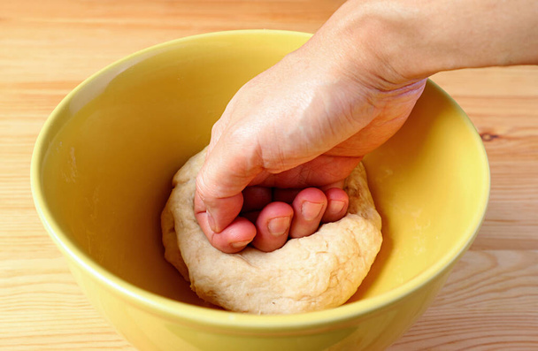 Κλείσιμο του χεριού του ανθρώπου που ζυμώνει ζύμη ψωμιού σε ένα μπολ ανάμιξης - Φωτογραφία, εικόνα