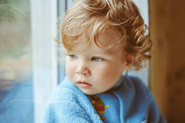 Küçük, ciddi bir çocuk pencerede oturuyor. - Fotoğraf, Görsel