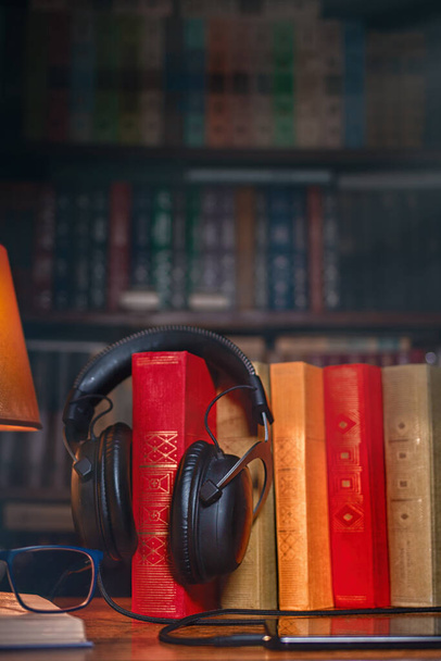 Op een houten tafel naast de lamp staan een koptelefoon, een telefoon, een stapel boeken en glazen. Het concept van moderne technologie en audioboeken. Sluiten.. - Foto, afbeelding