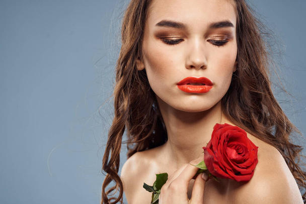 Женский портрет с красной розой рядом с лицом на сером фоне и макияж вьющиеся волосы - Фото, изображение