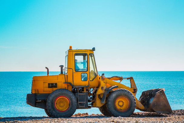Yellow bulldozer on the background of clear blue sky and sea. Copy space. Copy space and close up. - Photo, Image