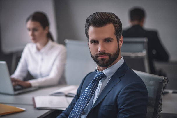 Attractive man sitting at table in office with colleagues - Photo, image