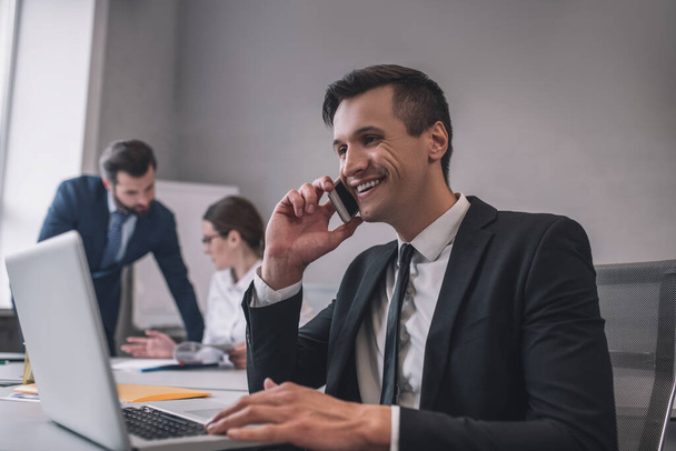 Hombre de negocios sonriente hablando en el teléfono inteligente en la oficina - Foto, imagen