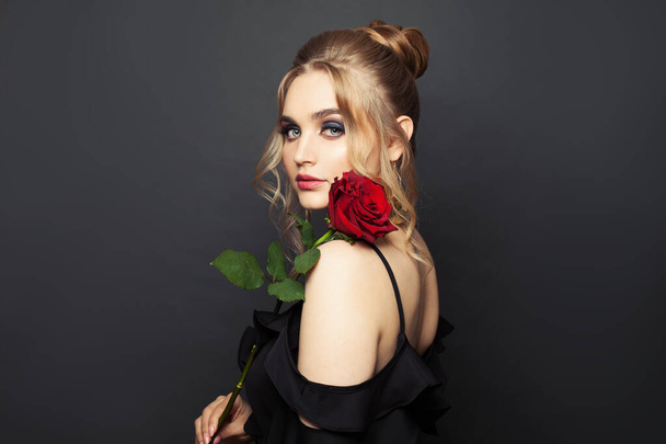 Pretty woman posing with red rose flower on black background - Foto, afbeelding