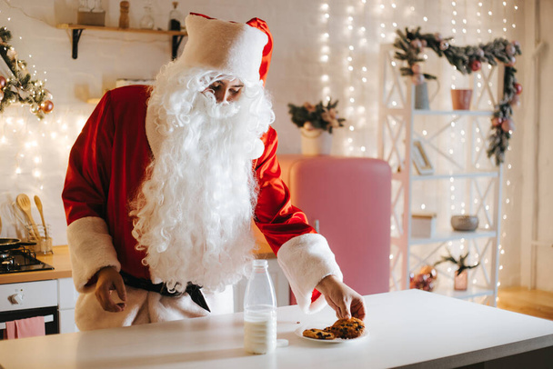 Kerstman die koekjes eet en melk drinkt met Kerstmis - Foto, afbeelding
