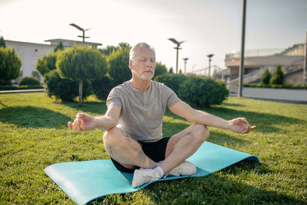 Grey-haired man sitting in lotus pose with hands in Gyan mudra - 写真・画像