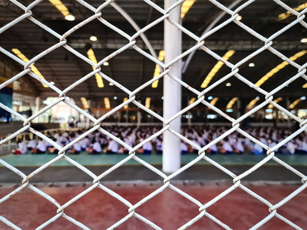 Full Frame Metal Fence met wazig Thaise studenten in uniform zittend op de vloer wachtend op het examen - Foto, afbeelding