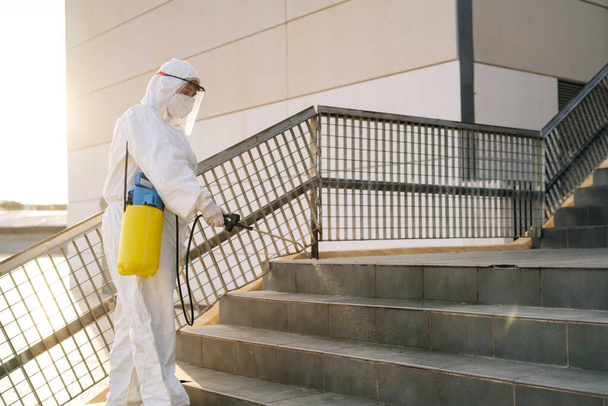 Man in virus protective suit and mask disinfecting buildings with the sprayer. - Foto, imagen