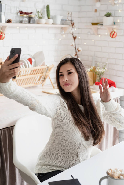 Молодая брюнетка болтает с друзьями по мобильному телефону на кухне - Фото, изображение