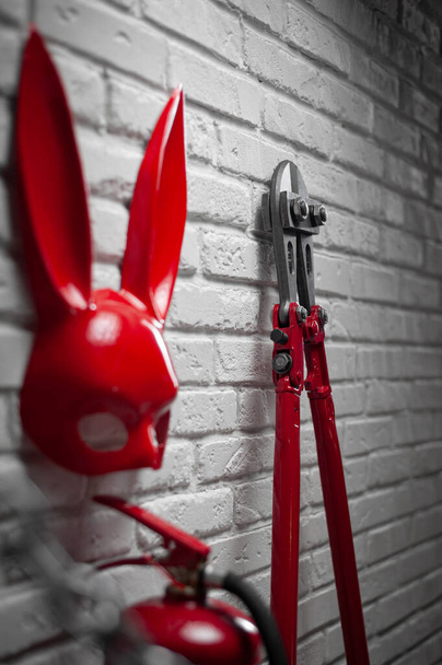 Tavşan maskesi, yangın söndürücü ve esnek zincirli cıvata makası olan bir tuğla duvarın yaratıcı tasarımı. - Fotoğraf, Görsel