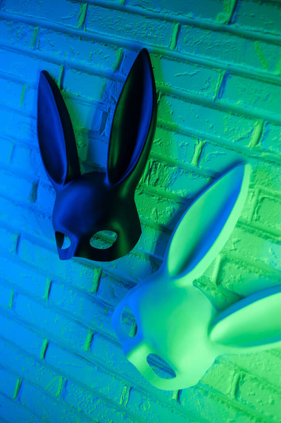 schwarz-weiße Kaninchenmaske auf weißem Wandhintergrund in neongrün-blau - Foto, Bild