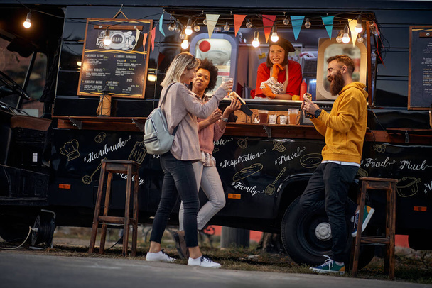 group of multiethnic young adult friends having fun while eating in front of modified truck for mobile fast food service - Fotó, kép