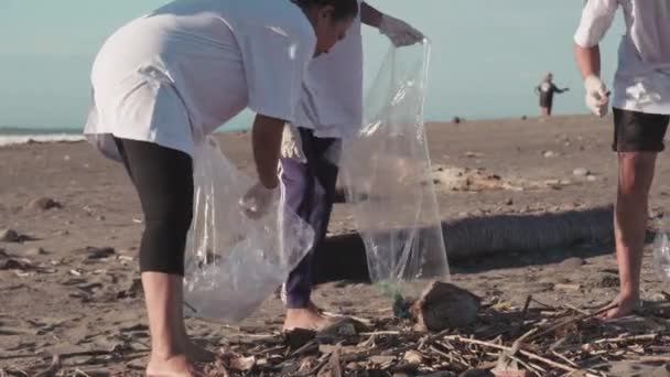汚染された雑然としたビーチをごみからきれいにすることに曲げられている若いインドネシアの環境保護主義者のグループは、地球を助けるために喜んでゴミ袋に入れます - 映像、動画