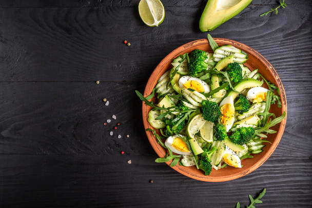 Avocado salad with boiled eggs, broccoli, spinach and almond nuts in bowl on dark background. - Photo, Image