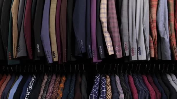 Férfi ruha klasszikus különböző öltönyök vállfák sorban ruhaüzlet plázában. Egy csomó jelmez van az állványokon. Üzleti és kiskereskedelmi koncepció. - Felvétel, videó