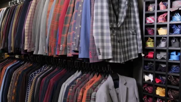 Roupa masculina ternos diferentes clássicos em cabides sucessivamente na loja de roupa no shopping. Muitas fantasias em prateleiras na loja. Conceito de negócio e varejo. - Filmagem, Vídeo