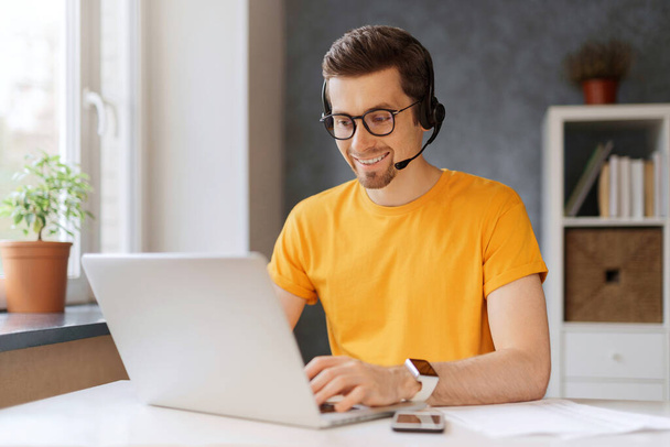 Happy programmer holding video call with colleagues clients partners.Call center operator works from home. Man in glasses wearing headphones, enjoying watching educational online webinar on laptop - Fotó, kép