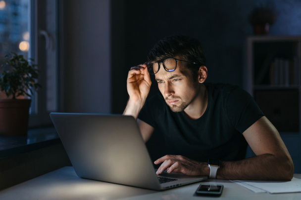 Aşırı çalışan serbest çalışan öğrenci geceleri dizüstü bilgisayarla çalışır. Gözlük takar, gözlerinde yorgunluk hisseder. Kuru gözlerde ağrı hisseder. Stres - Fotoğraf, Görsel