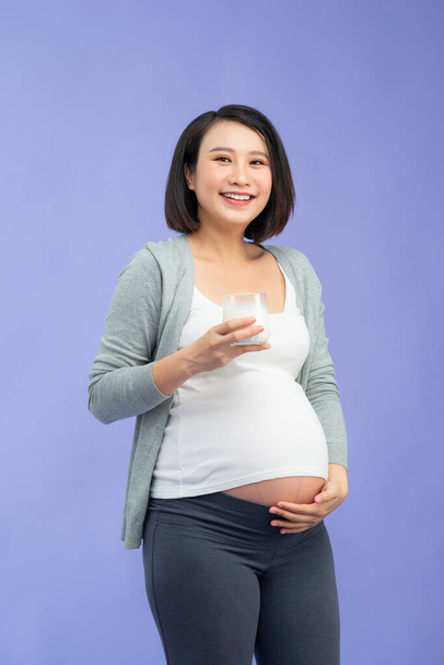Young pregnant woman with glass of milk over purple background - Valokuva, kuva