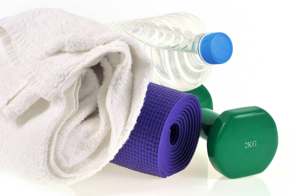Haltere ao lado de uma garrafa de água, toalha e tapete de ginástica enrolada  - Foto, Imagem