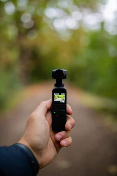 Προβολή Πορτραίτου Κρατώντας μια κάμερα τσέπης DJI Osmo Καταγράφοντας ένα θολό δάσος - Φωτογραφία, εικόνα