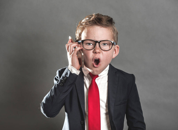 Злой детский босс кричит по мобильному телефону. Школьник в костюме, галстуке и очках как бизнесмен в офисе - Фото, изображение