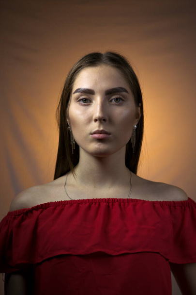 Portrait of a young woman in red top, standing in orange lit environment. - Foto, Bild