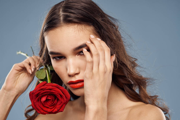 Retrato de una mujer con una rosa roja en sus manos sobre un fondo gris hombros desnudos maquillaje de noche - Foto, Imagen
