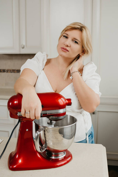 Güzel ev hanımı, mutfak malzemeleri kırbaçlanırken kırmızı bir miksere yaslanıyor. Bir kız lezzetli bir limonlu turta yapmaya hazırlanıyor.. - Fotoğraf, Görsel