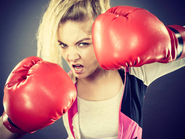 Sportieve boze vastberaden vrouw met rode bokshandschoenen, vechtend. Studio shot op donkere achtergrond. - Foto, afbeelding