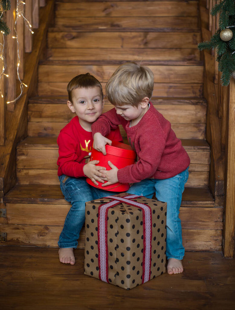dos lindos niños alegres pies desnudos de cuatro años de edad en suéteres rojos y vaqueros en una escalera de madera regalos abiertos. Nochebuena. Tiempo para la magia - Foto, imagen