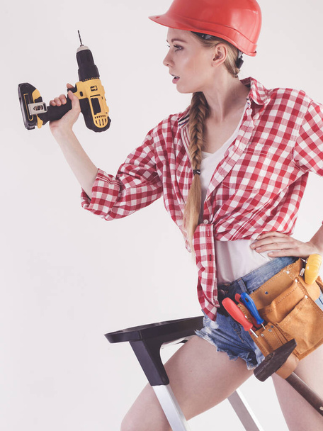 Young determinated woman using drill doing home renovation. Female construction worker having driller tool drilling wall. - Photo, image