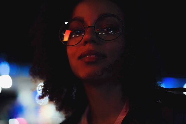 Portrait of young cute curly afro american girl. Night city lights. Neon illumination - 写真・画像