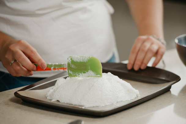 Close photo of the hands of a young woman who is improving with a scapula a shape of a big meringue on a tray. A girl is preparing to cook a delicious lemon meringue tart. - Foto, afbeelding