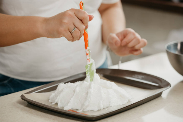 Foto der Hände einer jungen Frau, die mit einem Schulterblatt die Form eines riesigen Baiser auf einem Tablett verbessert. Ein Mädchen bereitet sich darauf vor, eine köstliche Zitronen-Baiser-Torte zu kochen. - Foto, Bild