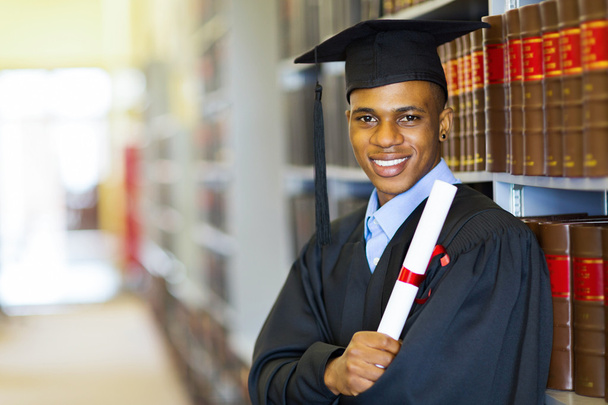Graduate leaned on bookshelf in library with diploma - Foto, Imagem