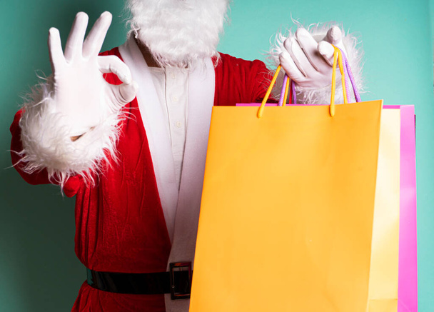 Close up of Santa Claus with gift bags giving ok with hand isolated on blue background. - Photo, Image